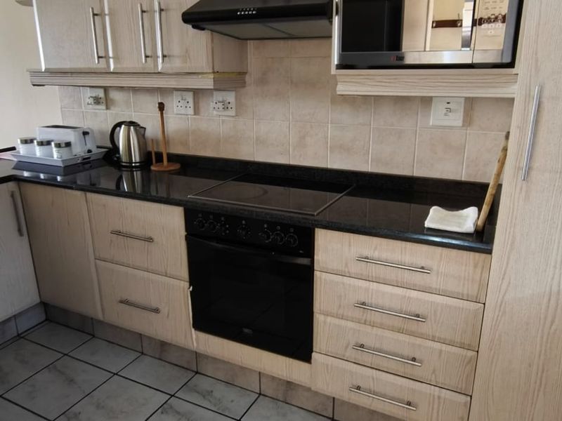 A functional kitchen featuring light wood cabinetry, dark granite countertops, a built-in electric oven and hob, and a tiled backsplash.
