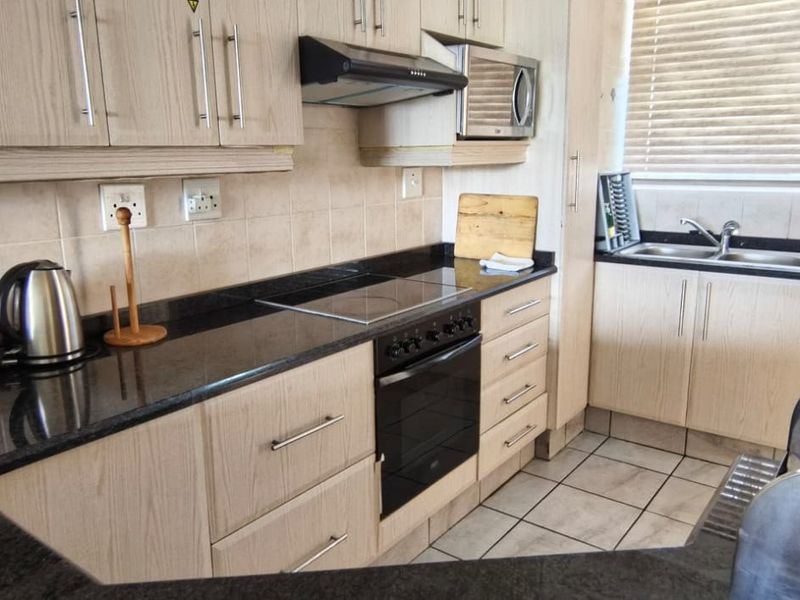 A functional kitchen featuring light wood-finish cabinetry, dark granite countertops, integrated appliances, and a tiled backsplash with a double basin sink.