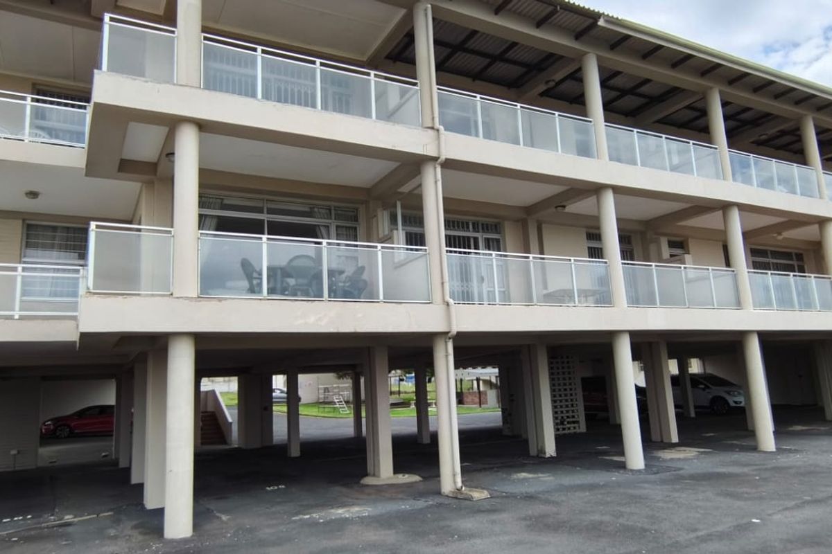 Exterior view of an apartment building featuring multiple balconies with glass balustrades and a covered ground-level parking area.