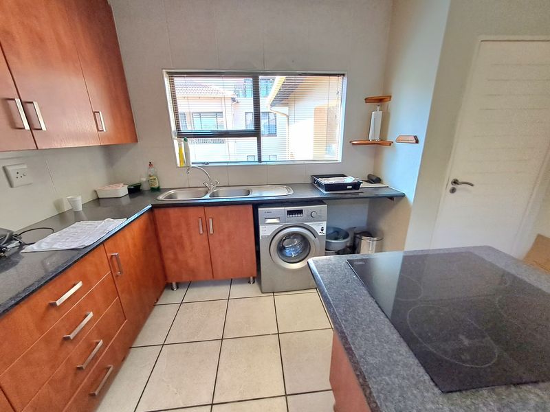 Functional kitchen featuring wood-finish cabinetry, stone-look countertops, integrated electric hob, and tiled flooring with space for a washing machine.