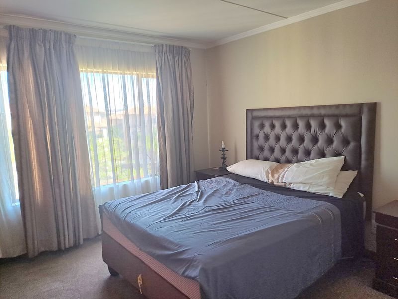 A well-lit bedroom featuring neutral wall tones, carpeted flooring, and large windows with installed curtain tracks.