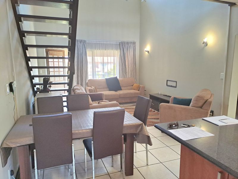Open-plan living and dining area featuring tiled flooring, a staircase, and a kitchen breakfast bar with granite countertops.