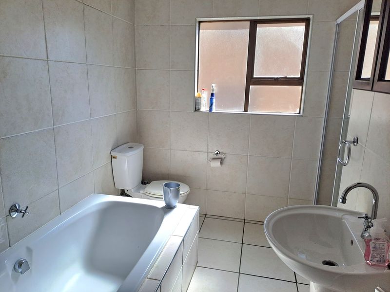 A functional bathroom featuring a bathtub, pedestal basin, and toilet with neutral wall and floor tiling and a frosted glass window for privacy.