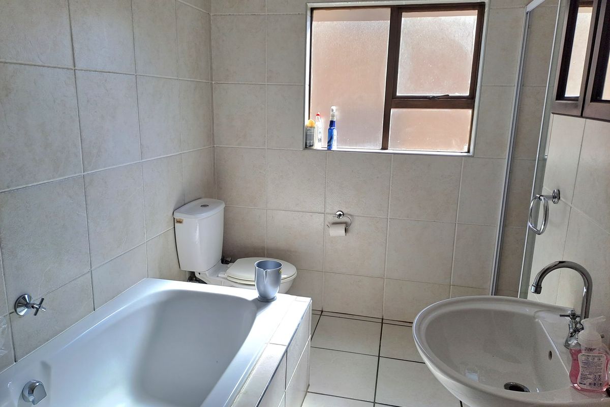A functional bathroom featuring a bathtub, pedestal basin, and toilet with neutral wall and floor tiling and a frosted glass window for privacy.