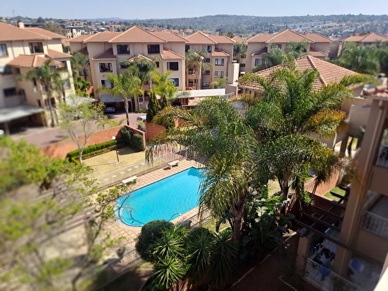 Elevated aerial view of the apartment complex featuring a communal swimming pool, landscaped gardens, and paved outdoor areas.