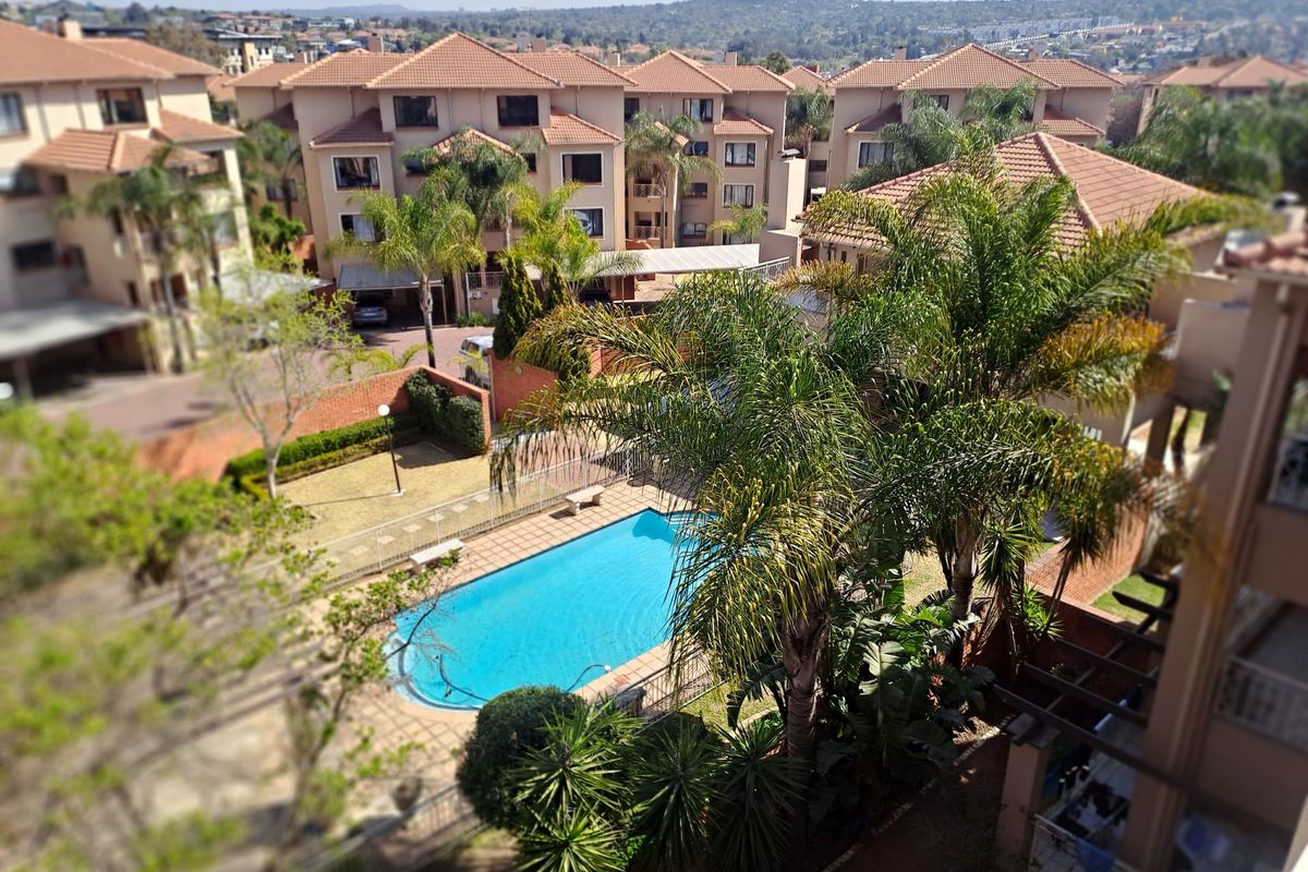 Elevated aerial view of the apartment complex featuring a communal swimming pool, landscaped gardens, and paved outdoor areas.