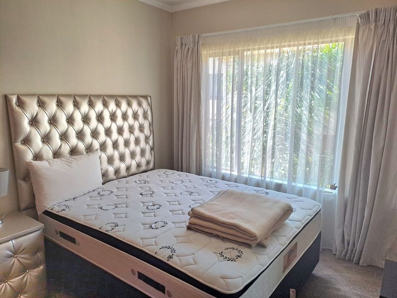 A well-lit bedroom featuring neutral wall tones, carpeted flooring, and large windows dressed with floor-to-ceiling curtains, providing a bright and comfortable living space.