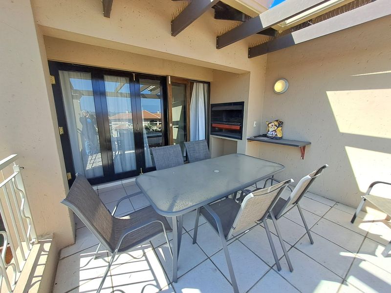 Covered balcony featuring a built-in braai, tiled flooring, and timber pergola, providing a functional outdoor entertainment space with direct access to the interior.