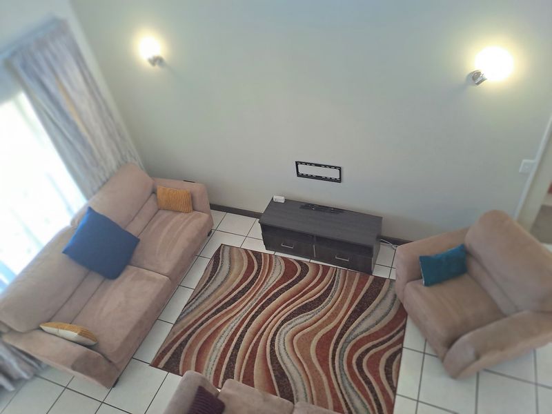 A high-angle view of a living room featuring tiled flooring, wall-mounted lighting, and a dedicated television mounting area.