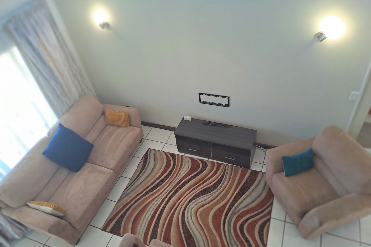 A high-angle view of a living room featuring tiled flooring, wall-mounted lighting, and a dedicated television mounting area.