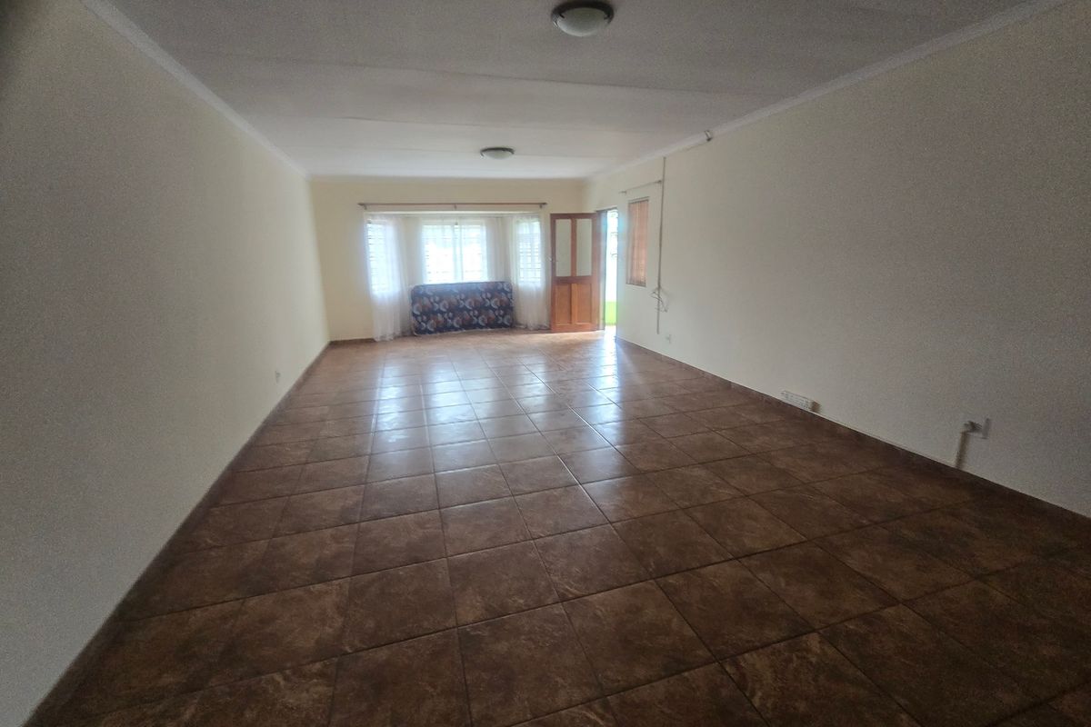 A spacious, empty living area featuring neutral walls, tiled flooring, and natural light from the rear door and windows.