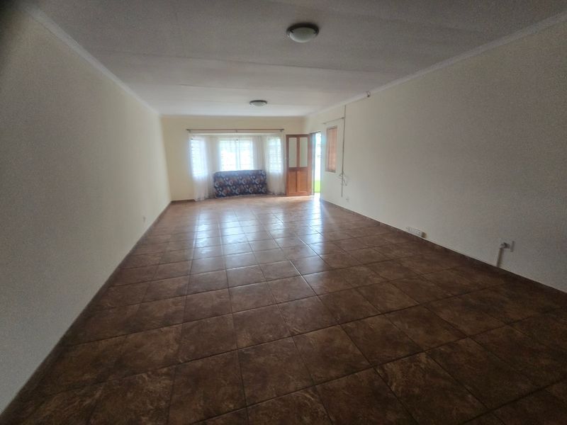 A spacious, empty living area featuring neutral walls, tiled flooring, and natural light from the rear door and windows.