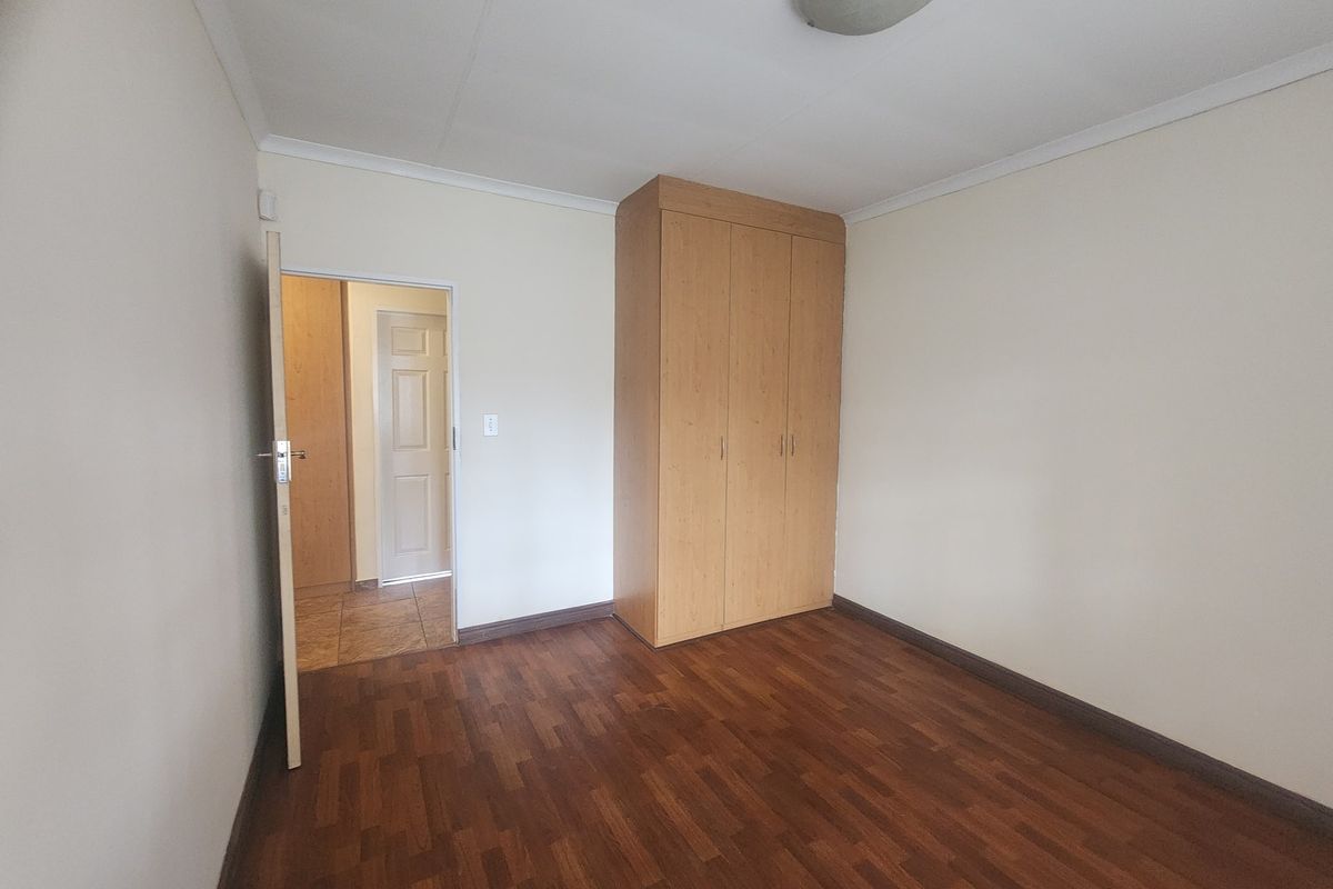 A clean, empty bedroom featuring laminate flooring, a built-in wardrobe, and neutral wall finishes, offering a blank canvas for personalization.