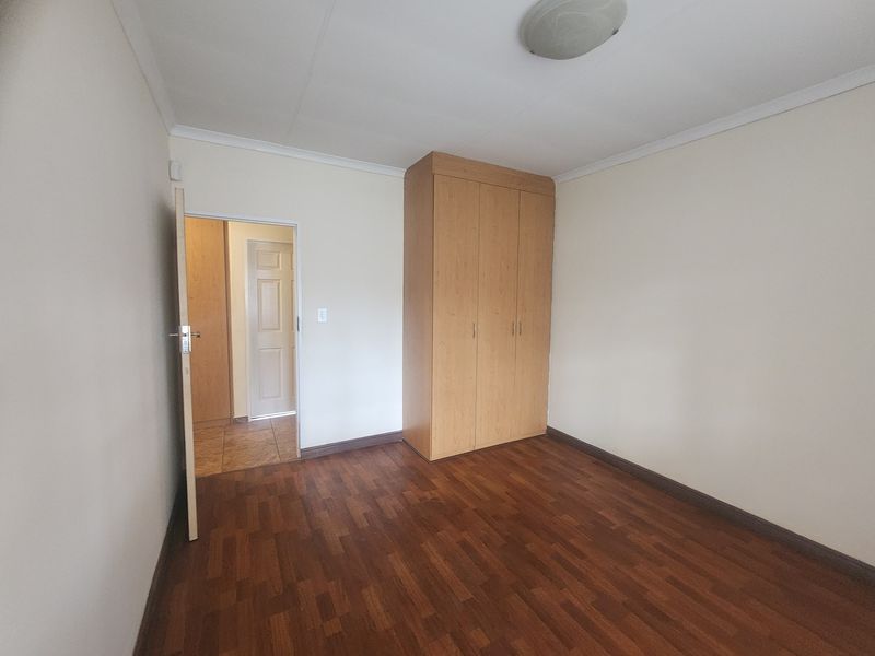 A clean, empty bedroom featuring laminate flooring, a built-in wardrobe, and neutral wall finishes, offering a blank canvas for personalization.