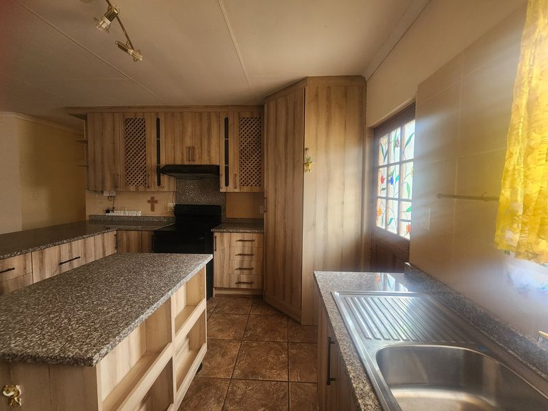 A functional kitchen featuring wood-look laminate cabinetry, granite countertops, a stainless steel sink, and a distinctive stained glass door leading outdoors.