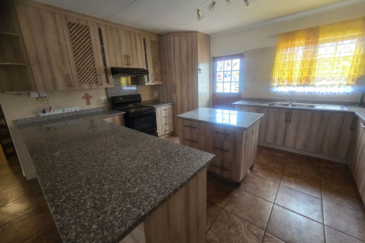 A functional kitchen featuring wood-look laminate cabinetry, granite countertops, a central island, and tiled flooring, providing ample workspace and storage.