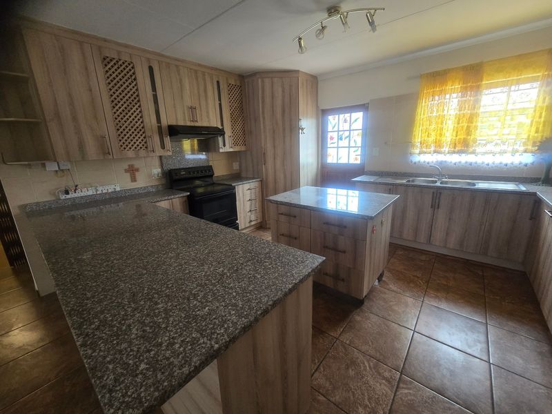 A functional kitchen featuring wood-look laminate cabinetry, granite countertops, a central island, and tiled flooring, providing ample workspace and storage.
