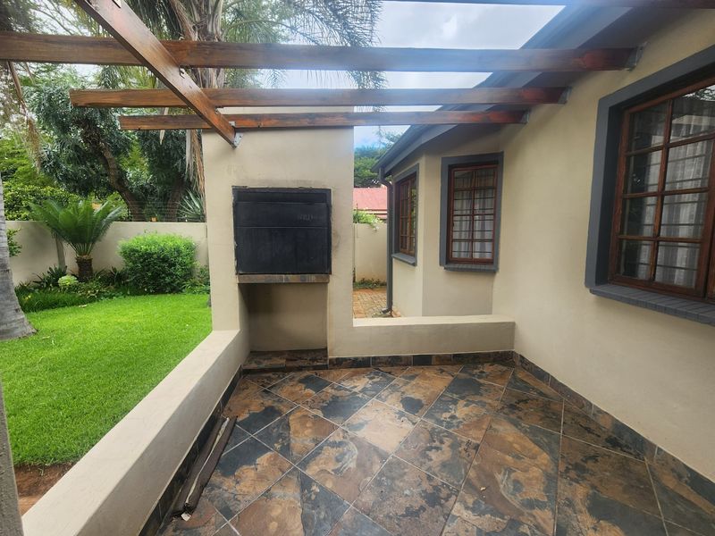 Covered patio area featuring a built-in braai, timber pergola structure, and slate tile flooring, overlooking a private garden space.