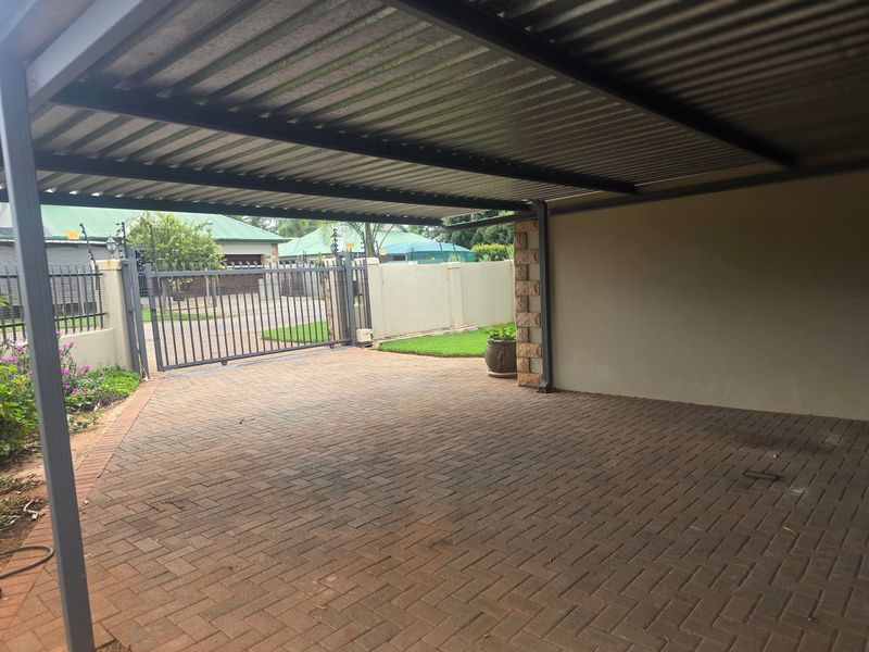A covered carport area featuring a corrugated metal roof, paved flooring, and a secure metal gate leading to the property entrance.