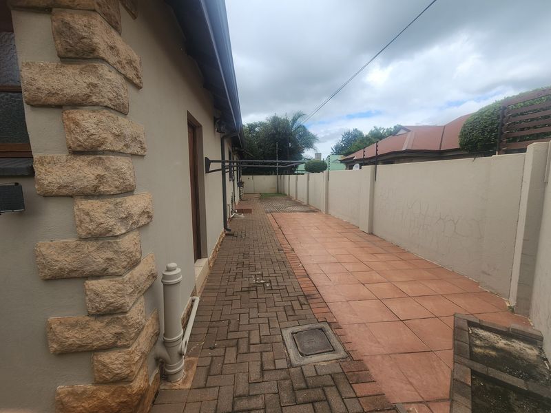 A side exterior view of the property featuring a paved walkway, tiled patio area, and a boundary wall with electric fencing.