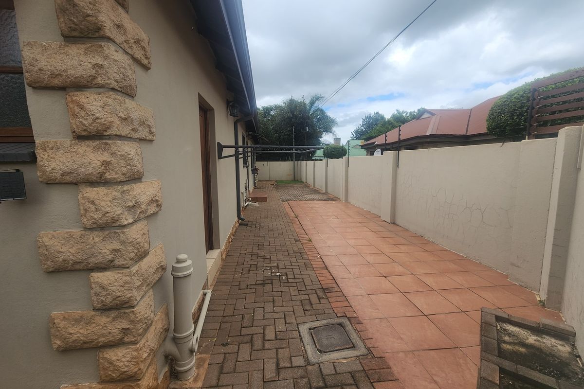 A side exterior view of the property featuring a paved walkway, tiled patio area, and a boundary wall with electric fencing.