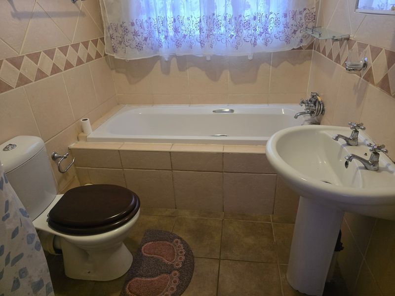A functional bathroom featuring a built-in bathtub, pedestal sink, and toilet with neutral ceramic wall and floor tiling.
