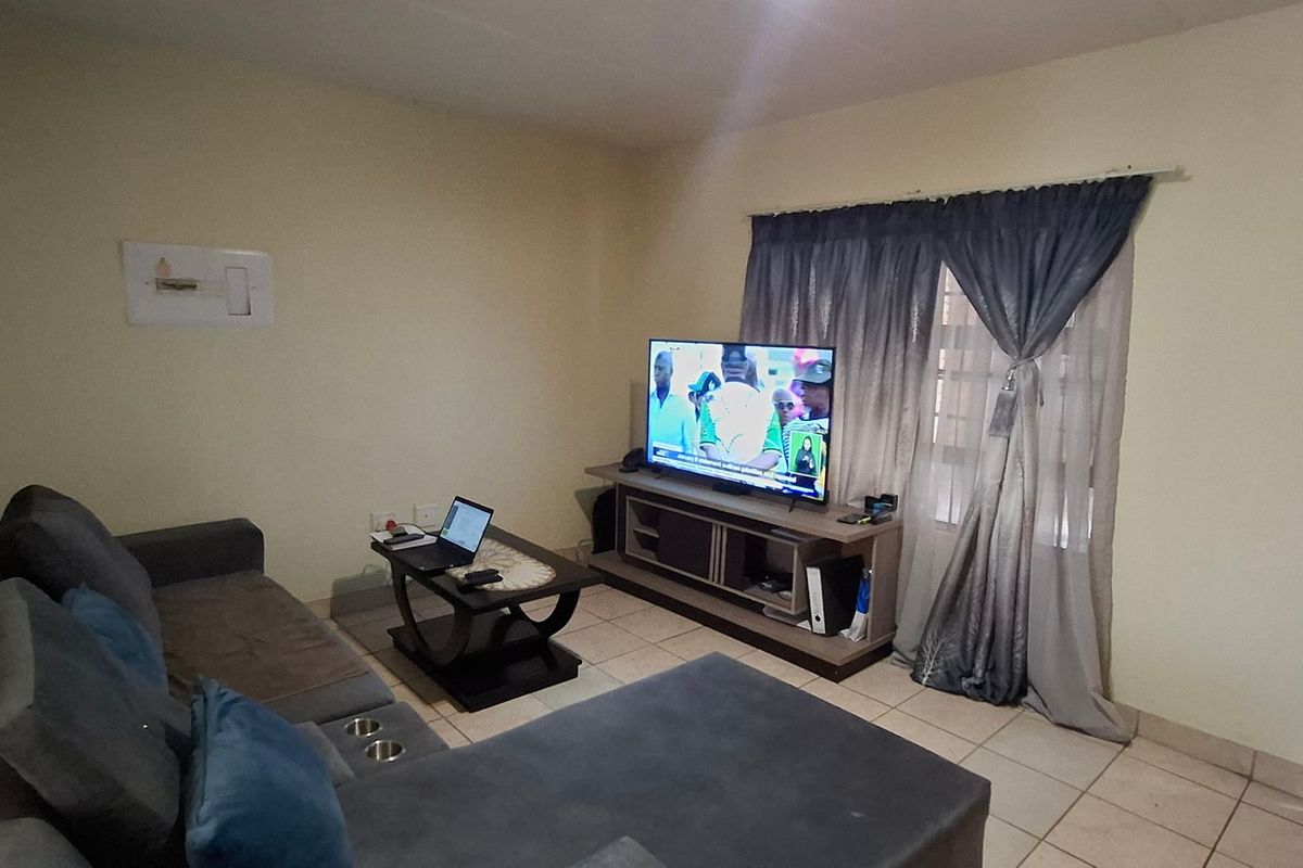 A functional living room featuring tiled flooring, a wooden entrance door, and a window with curtain fittings, offering a neutral base for interior updates.