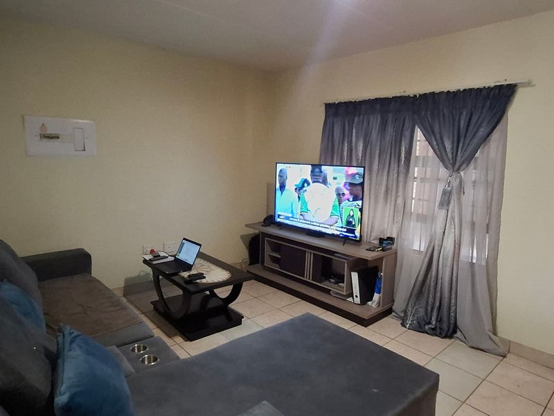 A functional living room featuring tiled flooring, a wooden entrance door, and a window with curtain fittings, offering a neutral base for interior updates.