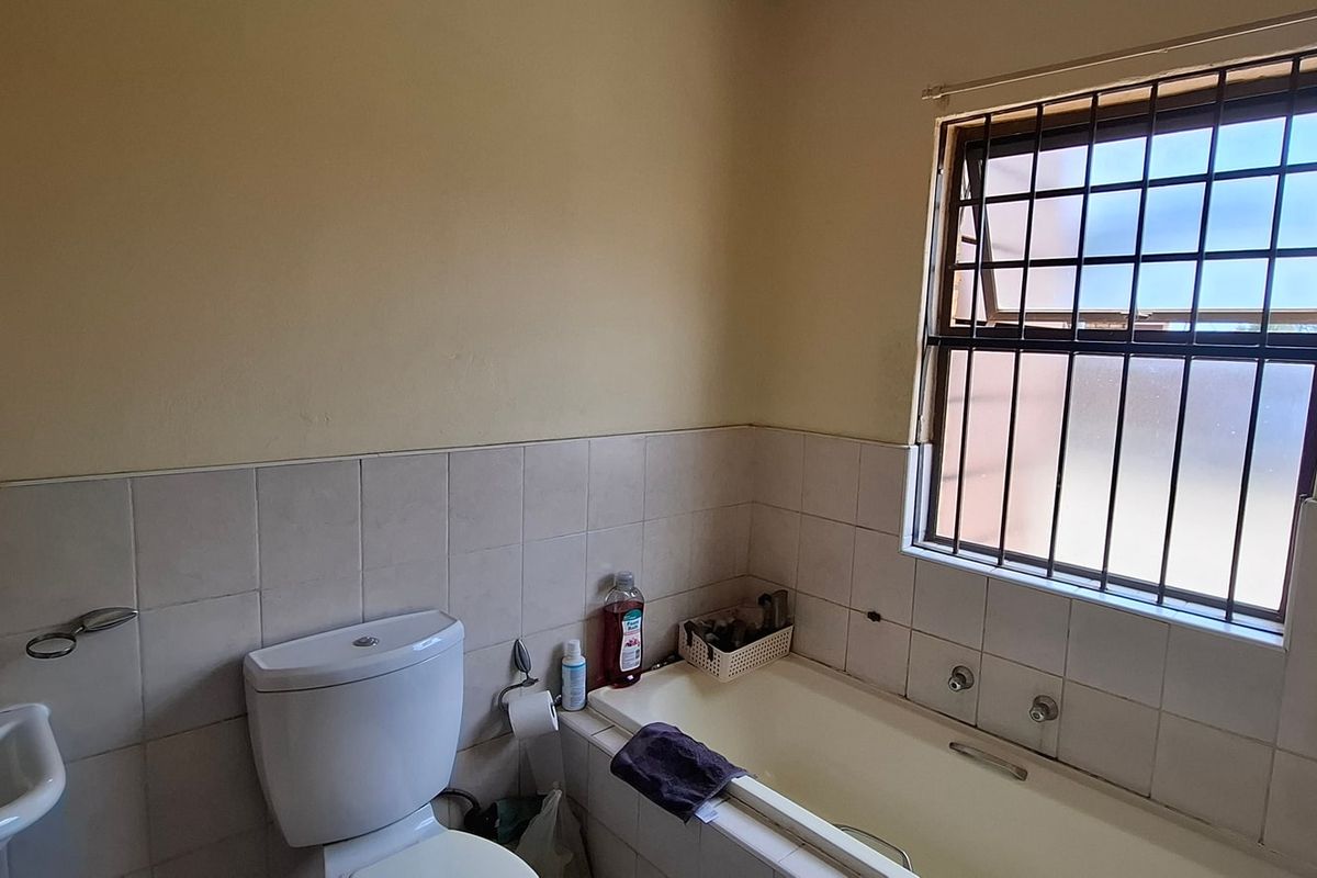 A functional bathroom featuring a bathtub, pedestal basin, and toilet, with tiled splashbacks and security bars on the window.