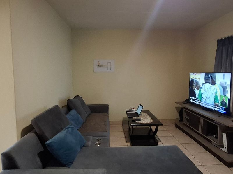 A functional living room featuring tiled flooring and a wall-mounted electrical distribution board, providing a neutral base for interior updates.
