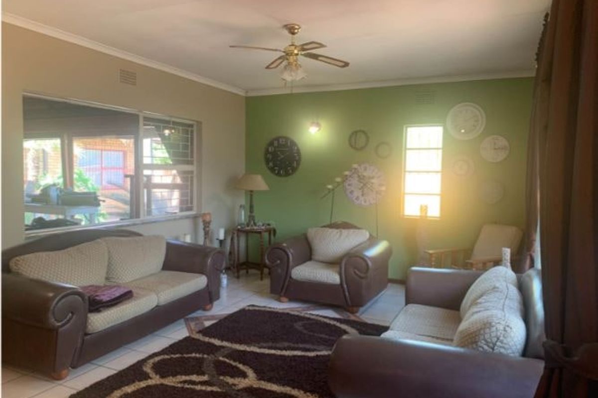 A comfortable living room featuring tiled flooring, a ceiling fan, and large windows with security bars, offering a bright and functional space.
