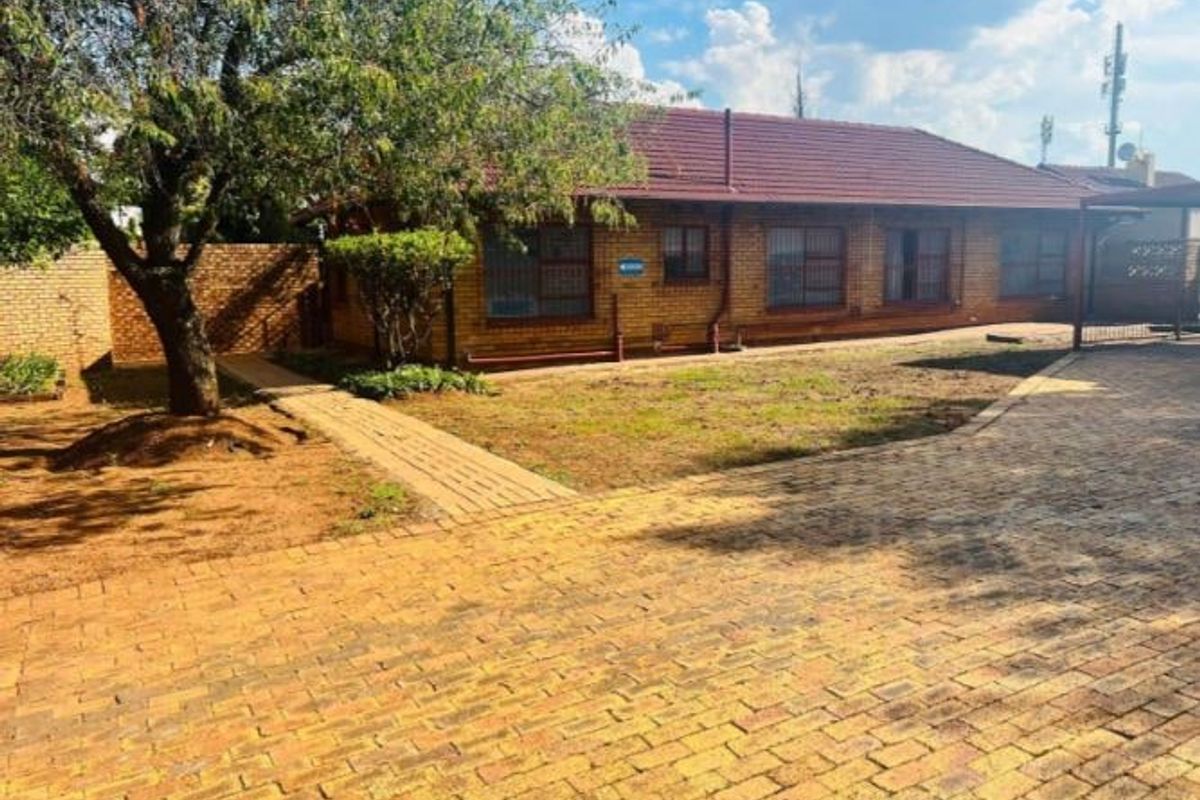 Rear view of a brick house featuring a tiled roof, paved driveway, and a garden area with a paved walkway.