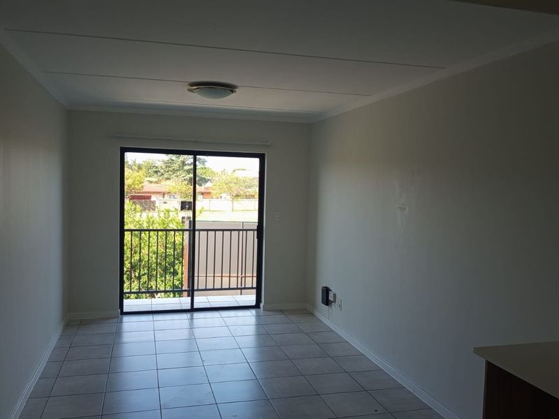 An empty open-plan living area featuring tiled flooring and a sliding glass door leading to a balcony.