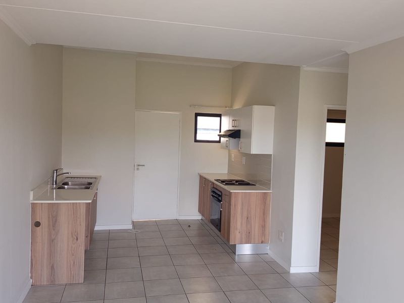 A clean, functional kitchen featuring built-in cabinetry, a stainless steel sink, integrated oven, hob, and extractor fan with neutral tiled flooring.