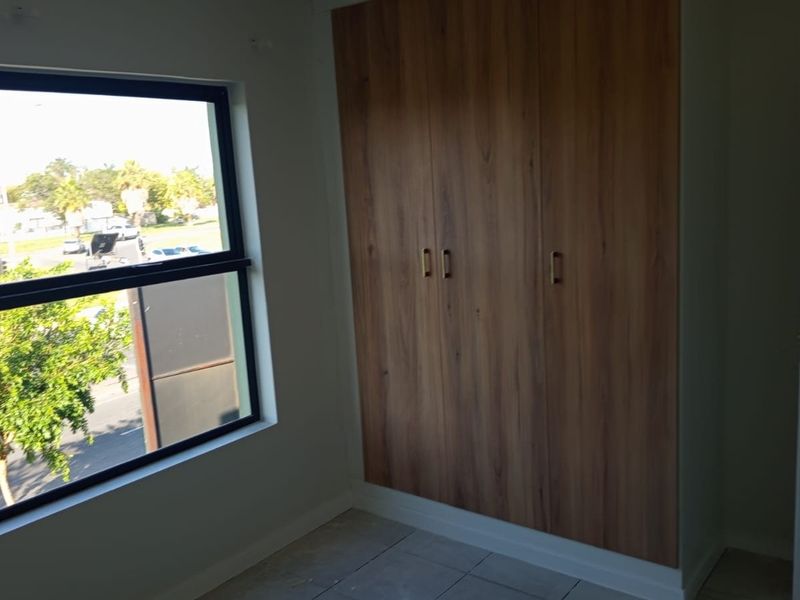 A bright, empty bedroom featuring modern wood-finish built-in cupboards, tiled flooring, and a large window with an exterior view.