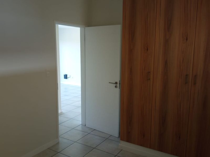A clean, empty bedroom featuring built-in wooden cupboards and neutral tiled flooring, offering a versatile space ready for personalization.