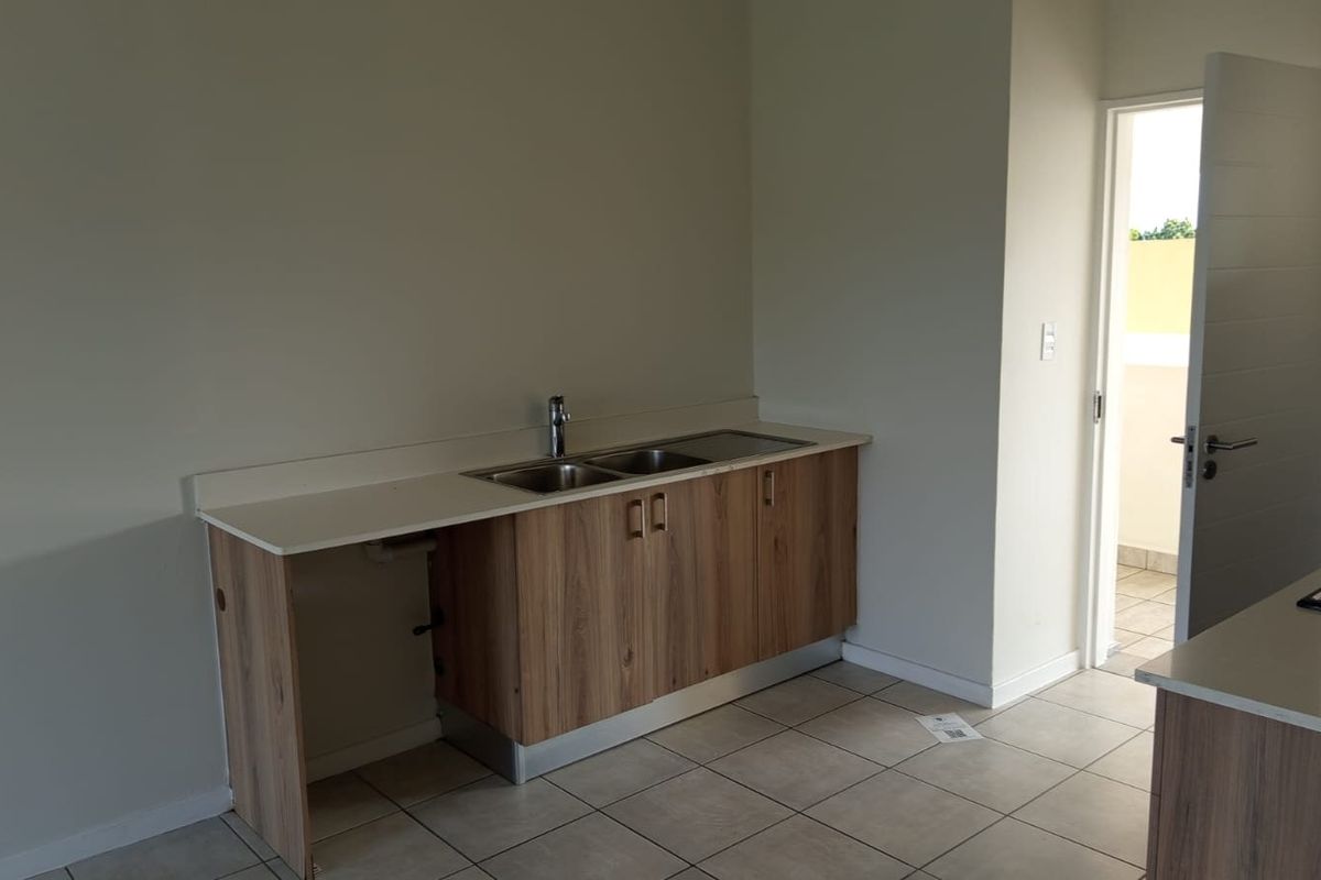 A clean, modern kitchen area featuring wood-finish cabinetry, a double sink, and tiled flooring, with an open layout leading to an outdoor space.