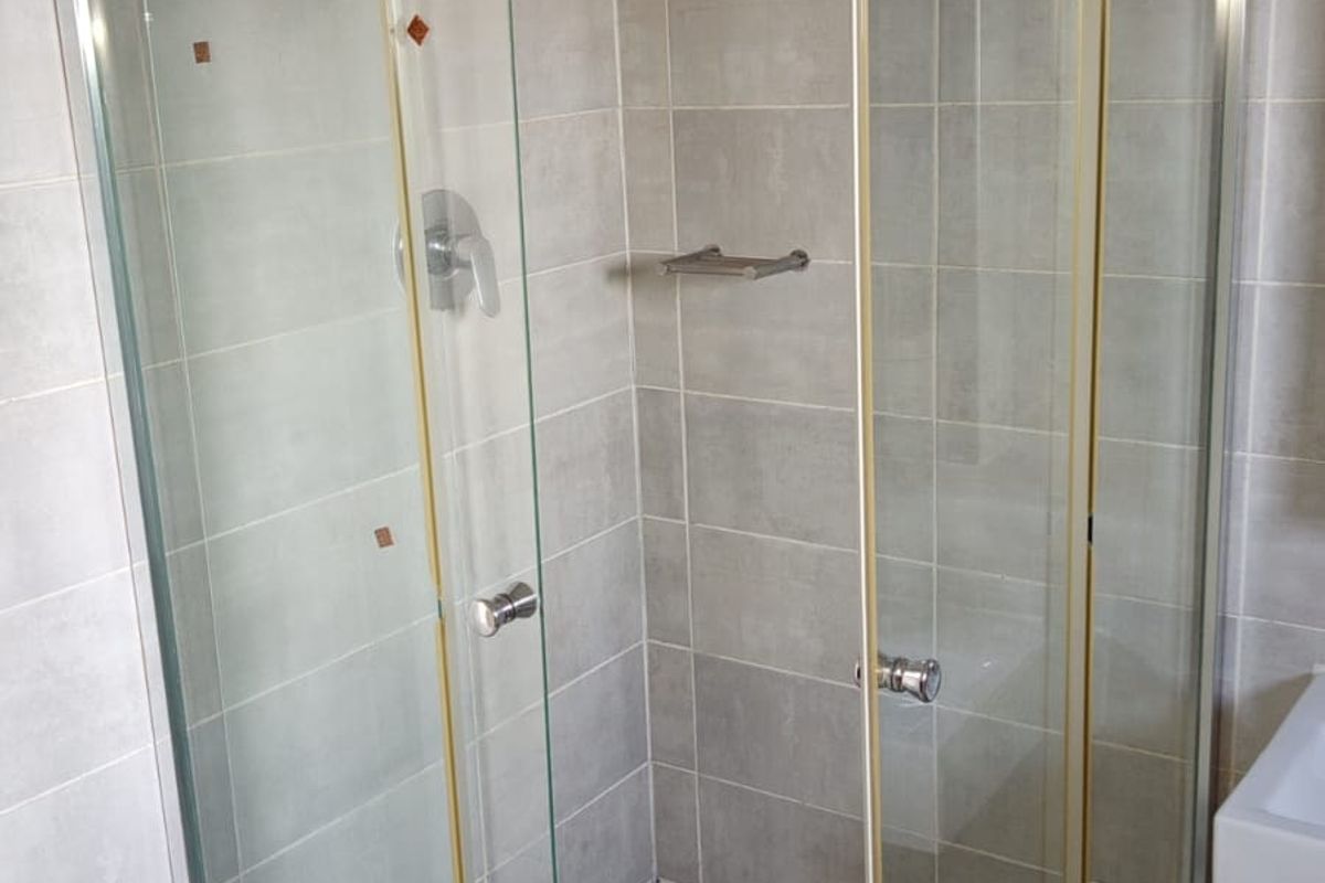 A functional corner shower unit featuring tiled walls and flooring, equipped with a standard shower mixer and glass enclosure.