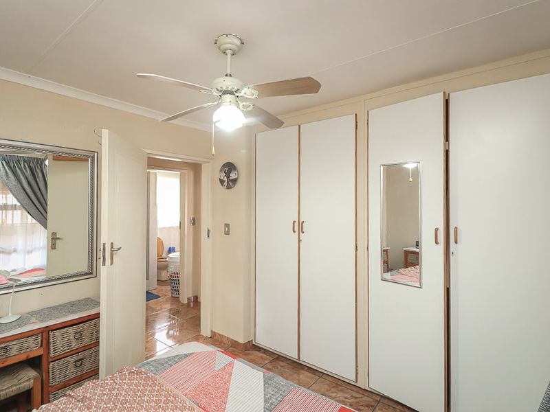 A bedroom featuring built-in cupboards, a ceiling fan, and tiled flooring, with an adjacent view into a bathroom.