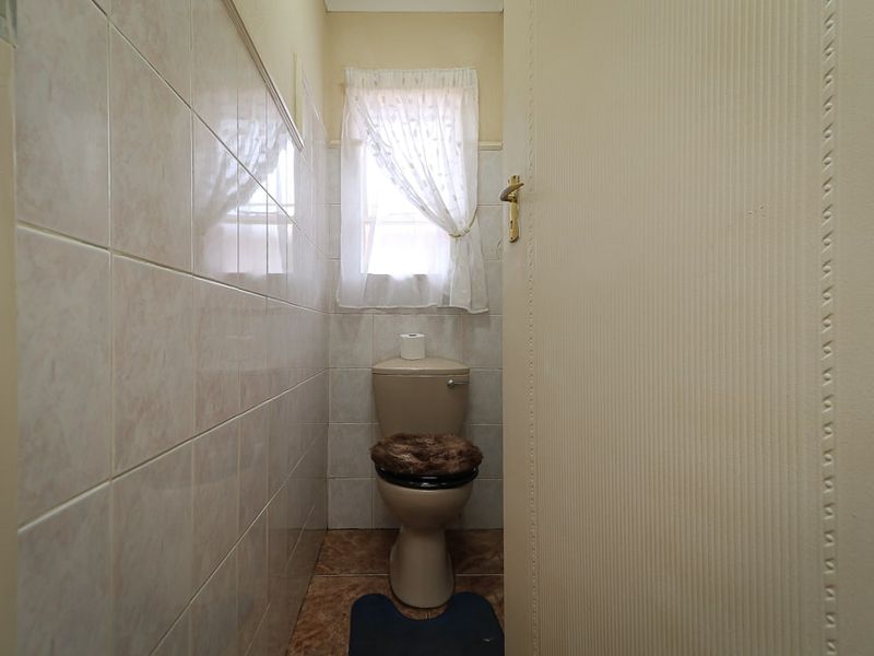 A compact guest toilet featuring neutral ceramic wall and floor tiling, providing a functional and clean space.