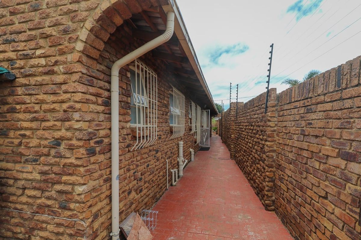 A side exterior walkway featuring face brick walls, security bars on windows, and electric fencing along the boundary wall.