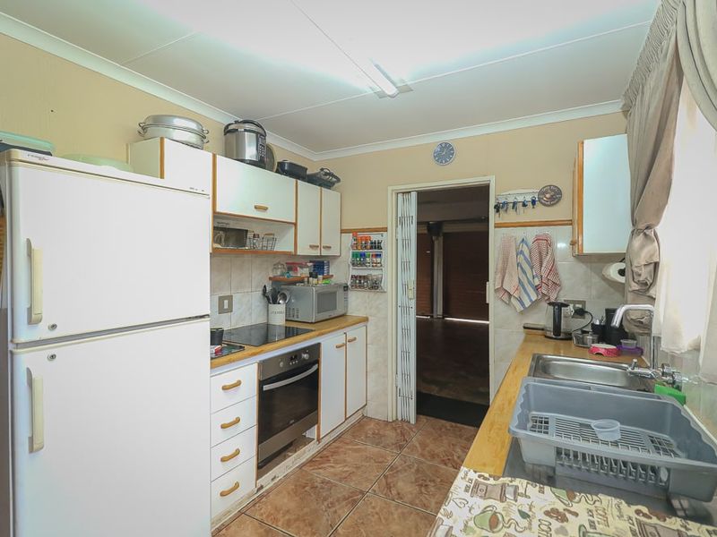 A functional kitchen featuring built-in cabinetry, an electric hob, an oven, and a stainless steel sink with tiled flooring and backsplash.