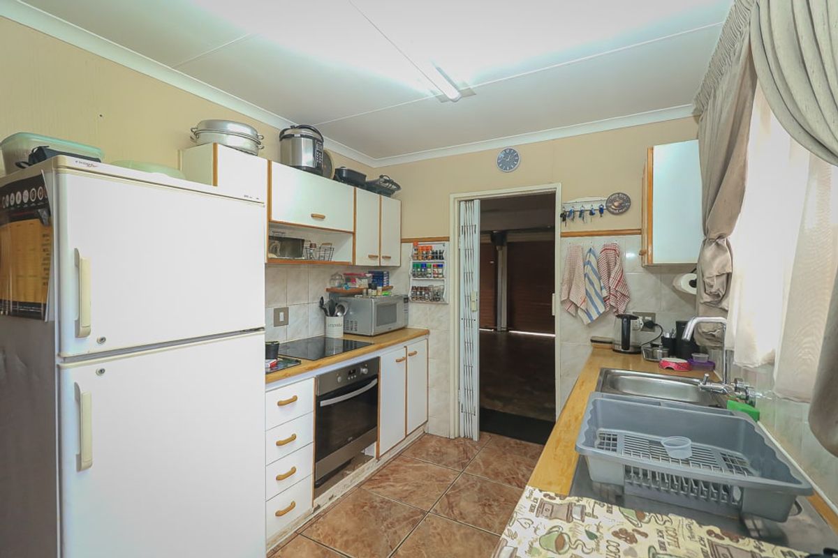 A functional kitchen featuring built-in cabinetry, an electric hob, an oven, and a stainless steel sink with tiled flooring and backsplash.