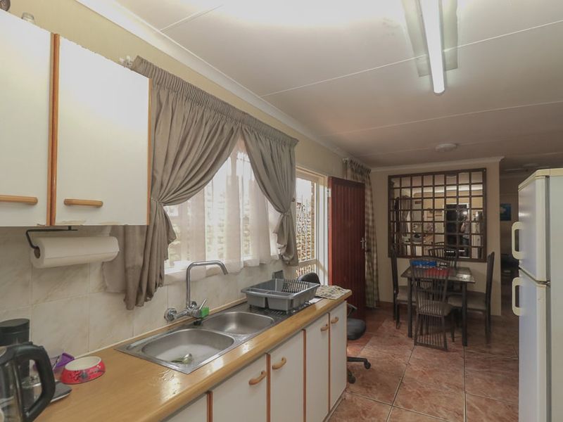 A functional kitchen featuring laminate countertops, a double bowl sink, tiled splashbacks, and built-in cabinetry, with an adjacent dining area.