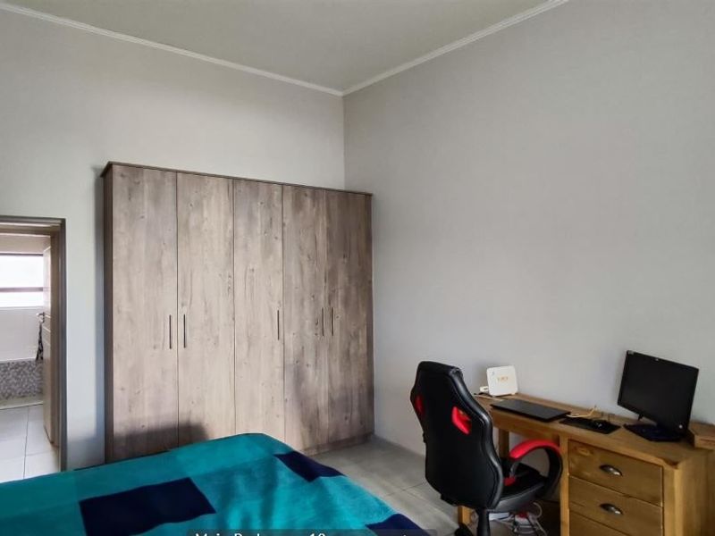 A bedroom featuring neutral walls, tiled flooring, and a large built-in wardrobe, with an adjoining bathroom visible through the doorway.