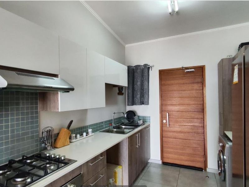 Modern kitchen featuring white and wood-tone cabinetry, gas hob, extractor fan, tiled backsplash, and direct access to an exterior door.