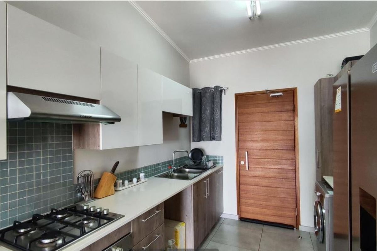 Modern kitchen featuring white and wood-tone cabinetry, gas hob, extractor fan, tiled backsplash, and direct access to an exterior door.