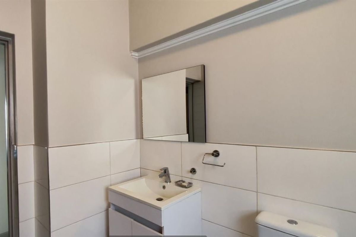 A clean, modern bathroom featuring a white vanity cabinet with basin, wall-mounted mirror, and toilet with tiled splashback.