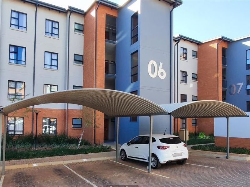Exterior view of a modern multi-story apartment complex featuring covered parking bays and well-maintained brick and painted facade finishes.