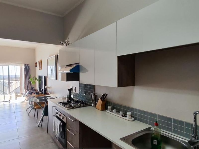 Modern open-plan kitchen featuring sleek white cabinetry, gas hob, and integrated appliances, flowing seamlessly into a bright living area with sliding door access.
